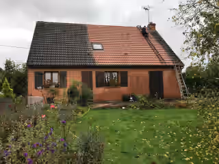 Toiture de pavillon à moitié démoussée : versant noirci à gauche, tuiles nettoyées à droite